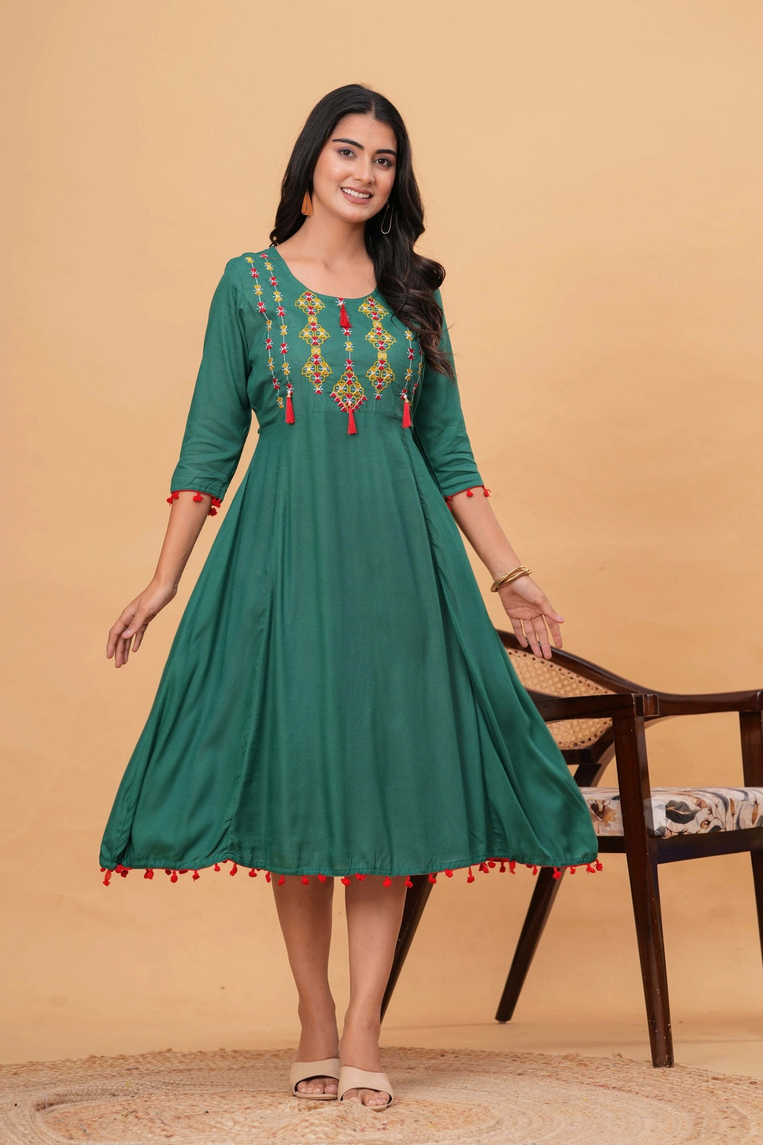 Deep green rayon flared kurta dress with multicolored embroidered yoke, red tassels, and red pom-pom lace detailing on sleeves and hem